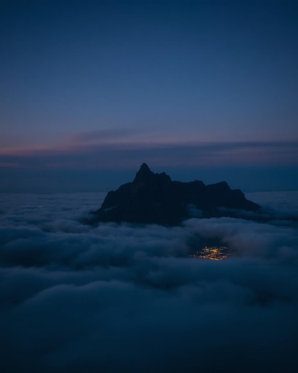 Table Mountain rising above cloud at dusk with Cape Town lights below
