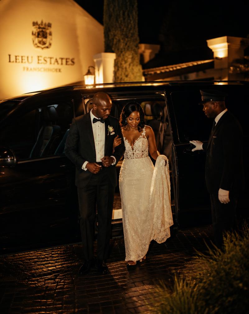 Bride and groom stepping out of a black Mercedes V-Class with a chauffeur at a wedding venue